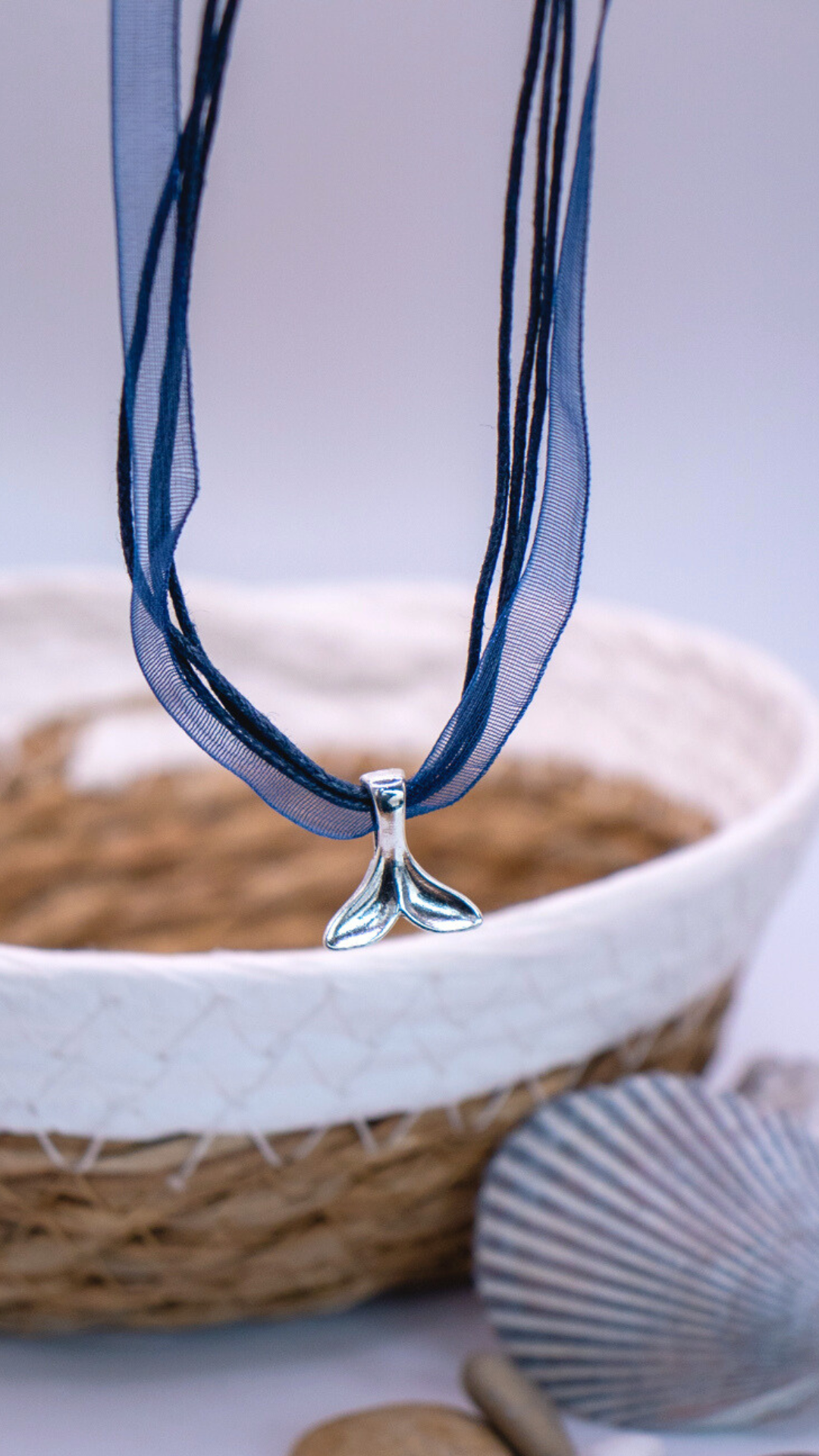 Necklace with a metallic whale tail pendant on multiple strands, including a blue ribbon and dark blue cords.