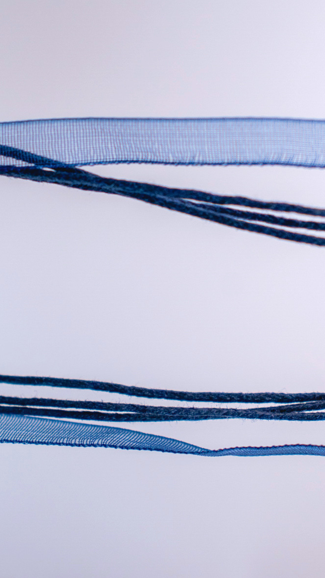 Necklace with a metallic whale tail pendant on multiple strands, including a blue ribbon and dark blue cords.