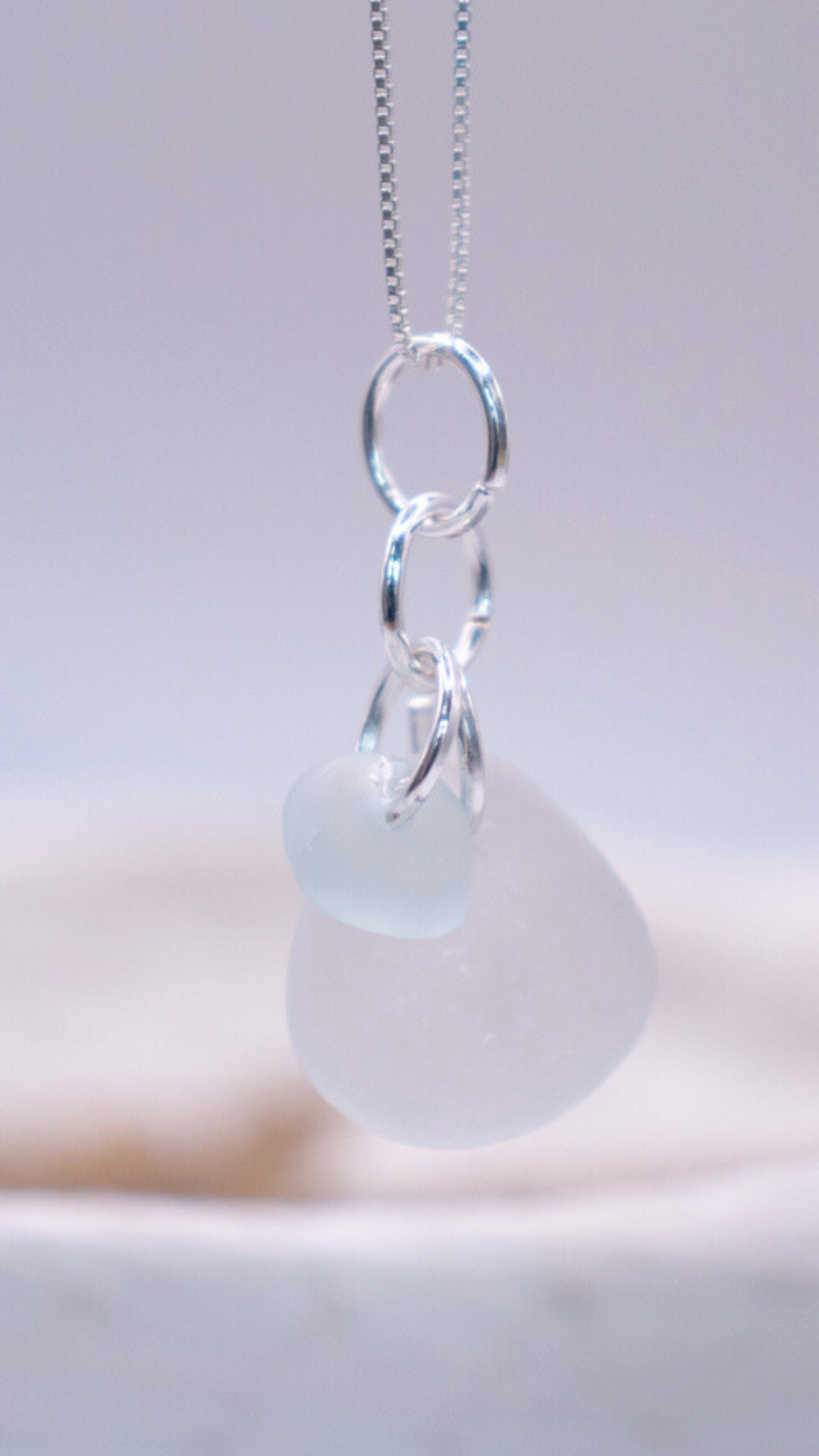 Necklace with a thin silver chain featuring two frosted pendants, one white teardrop-shaped and the other light blue.